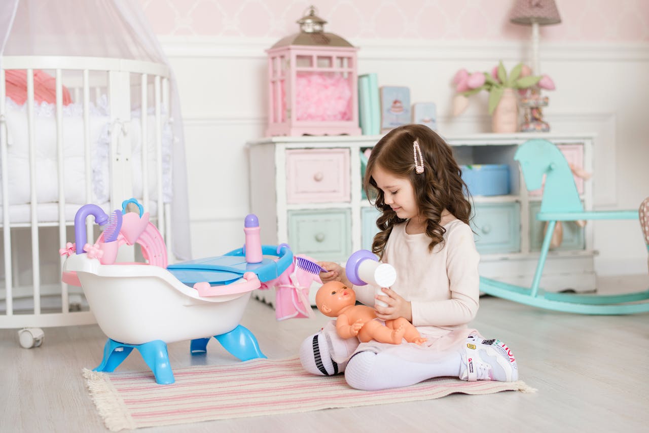 our-services-03 Young girl playing with a doll in a pastel-colored nursery room, surrounded by toys and decor.