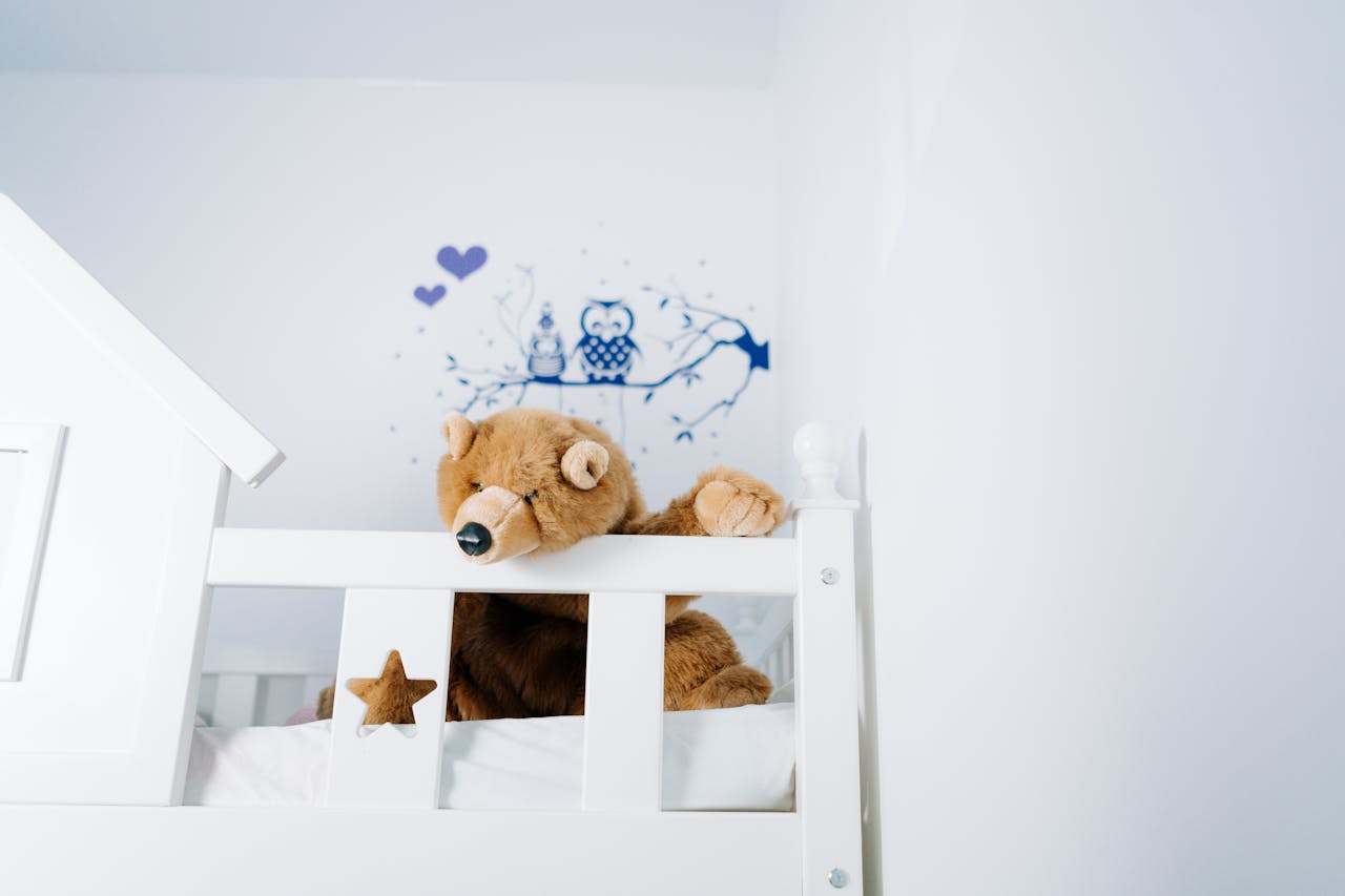 hero-gallery-02 A plush teddy bear rests on a child's bed with charming owl-themed wall art.